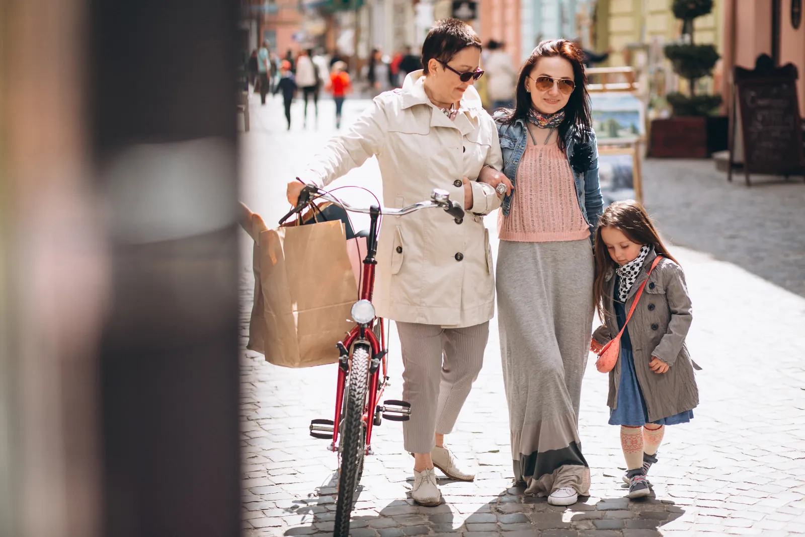 Grandmother, mother and daughter walking down a shopping street with a bike and shopping bags.