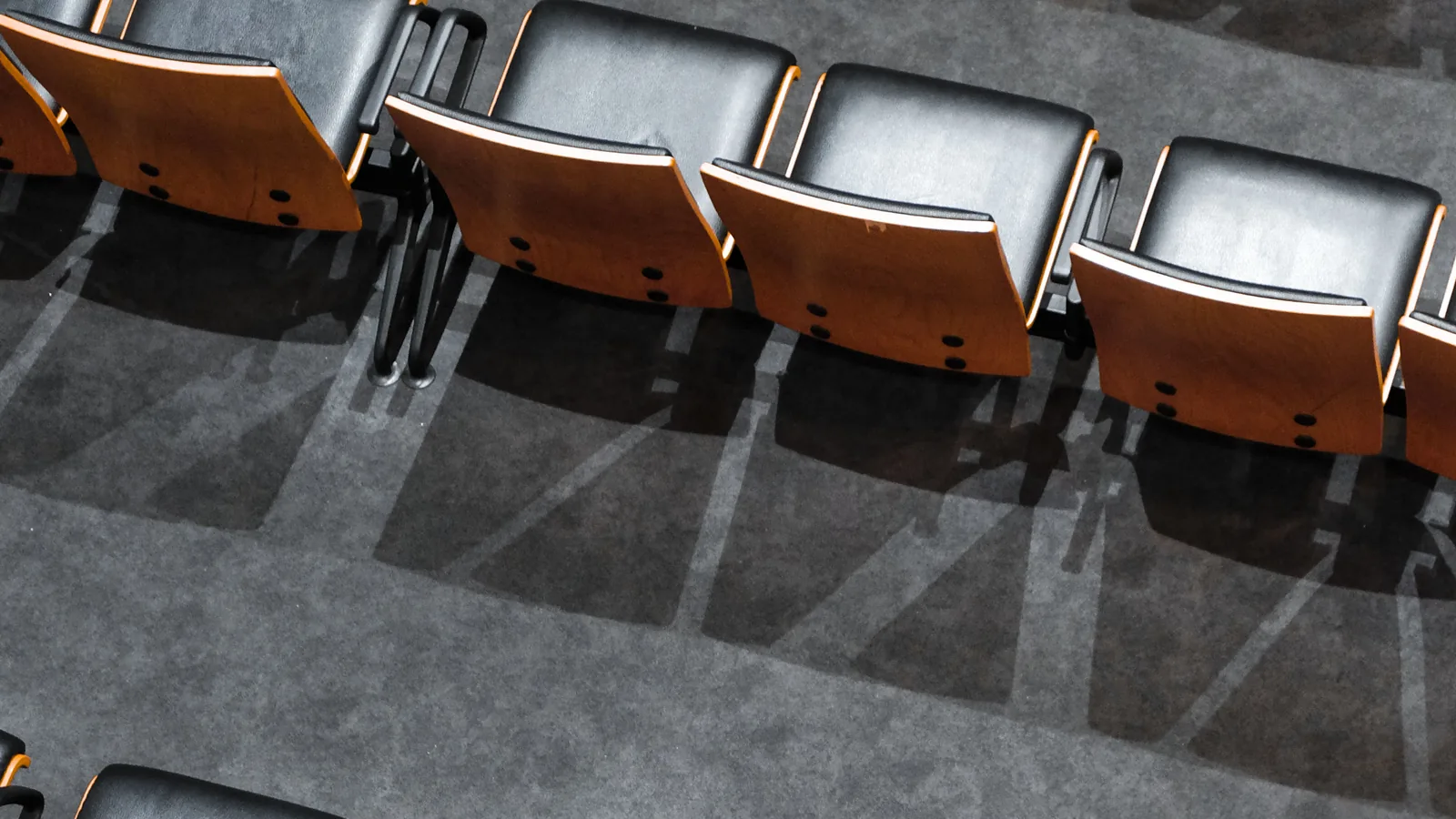 A row of empty seats seen from above, with long shadows on a grey floor.
