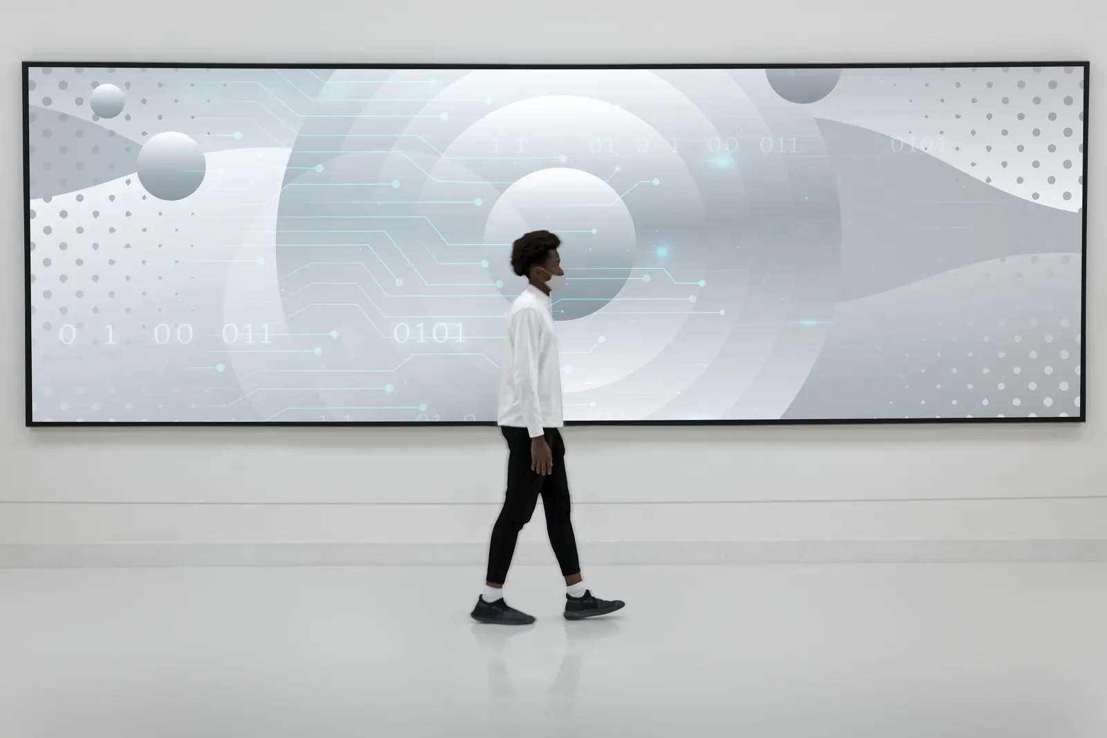 Man in white walking past a large light-grey screen with an abstract data chart.